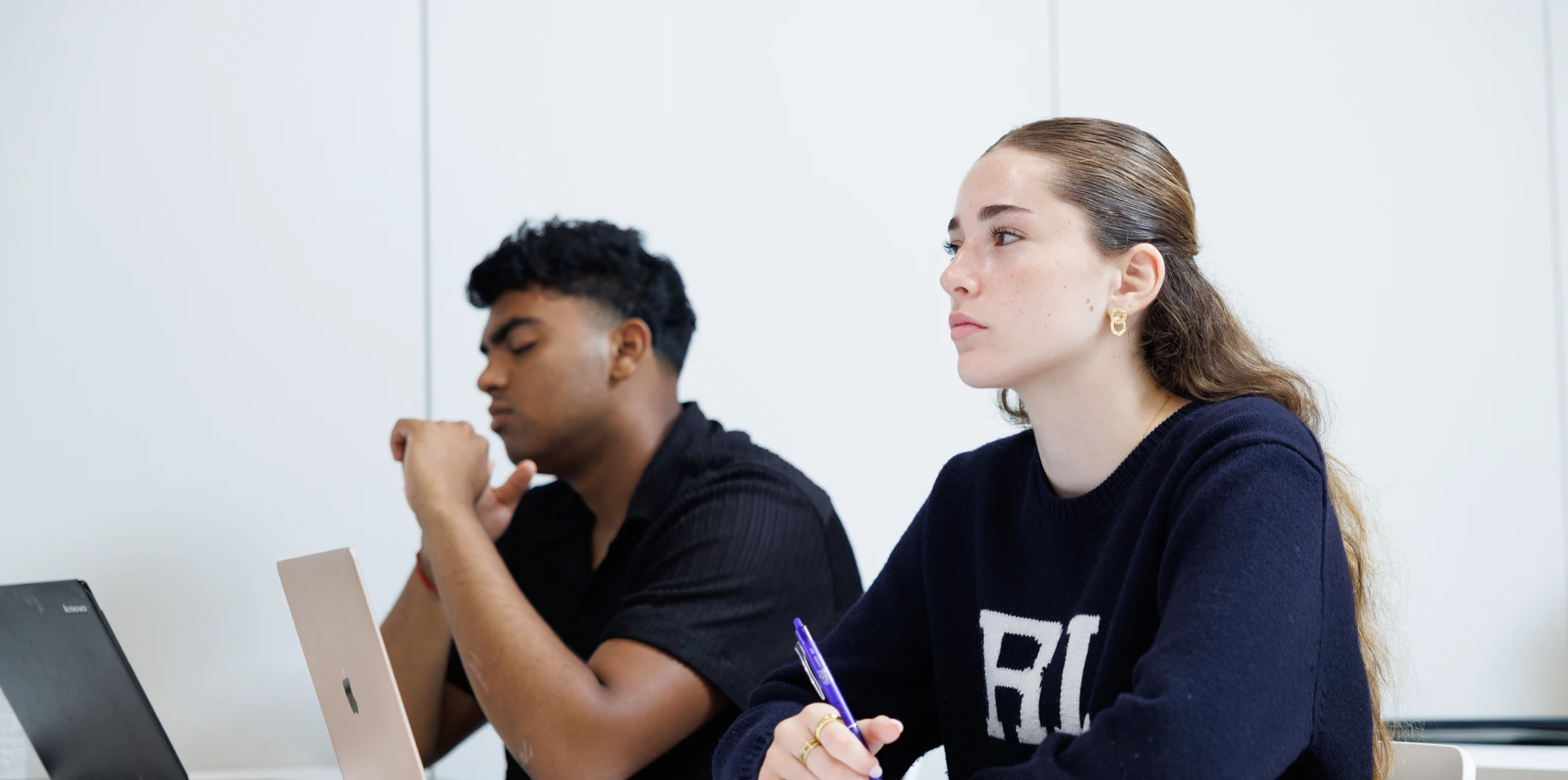 Two teenagers sitting at a desk with laptops